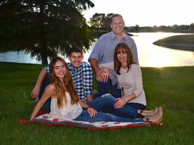 The Tracy family, founders of All-Pro Plumbing, smiling and sitting together outdoors by Emerald lake in Kokomo, IN