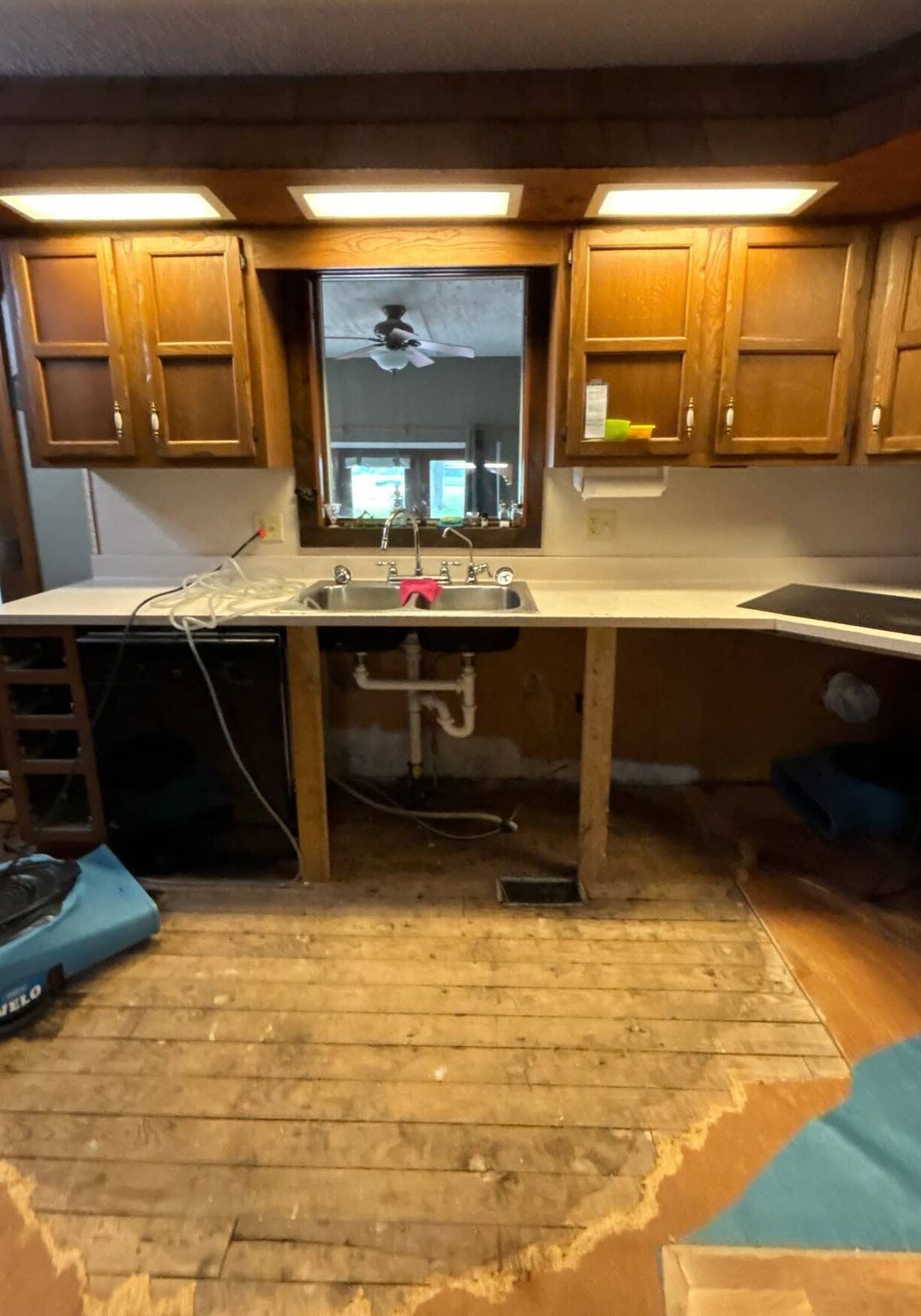 Kitchen with flooring removed and water damage remediation fans, showing effects of a sink plumbing leak, ready for repair by All-Pro Plumbing in Kokomo, IN