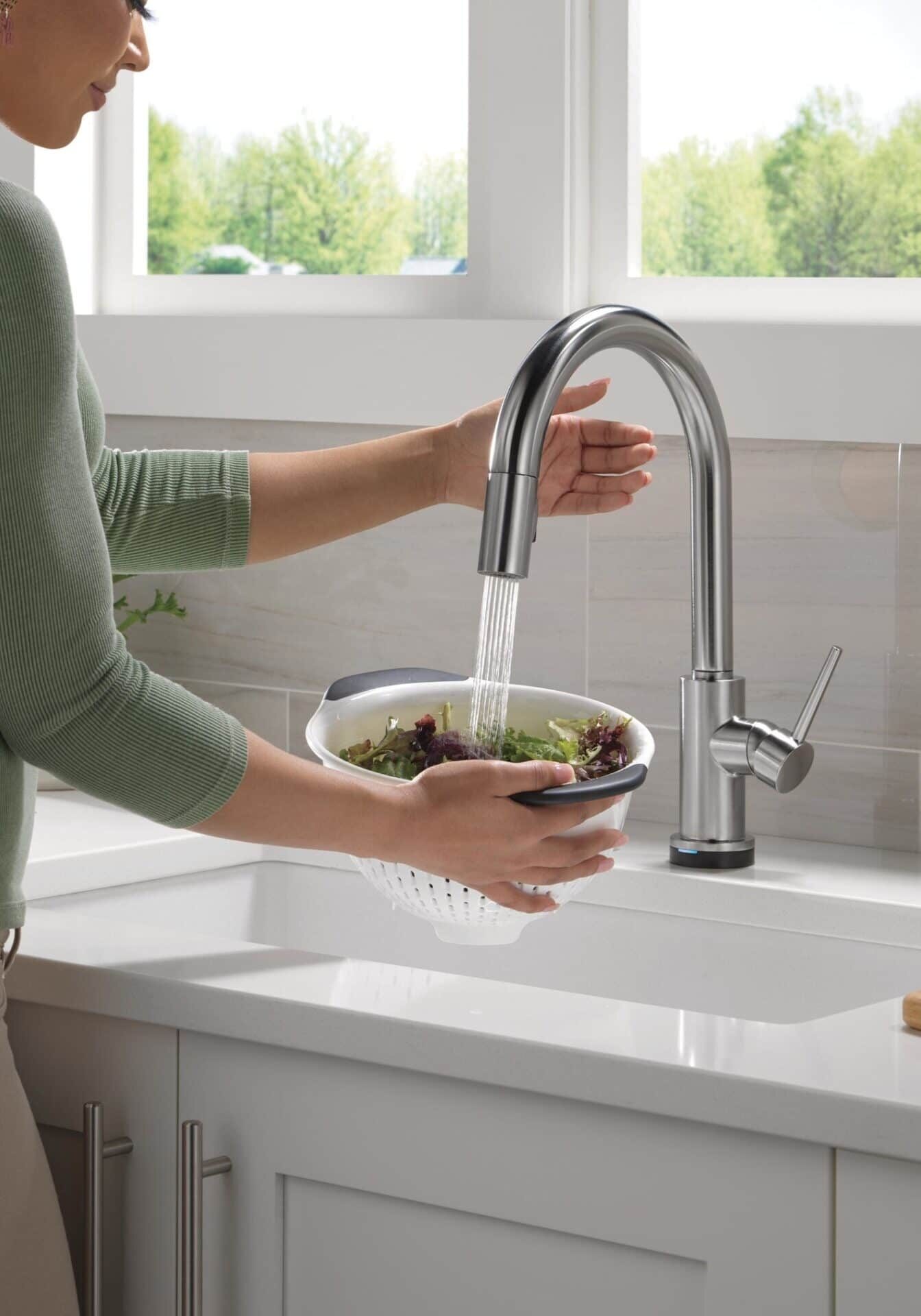 Woman washing fresh lettuce under a modern Delta Trinsic kitchen faucet, representing the benefits of clean, soft water for cooking and a healthier home provided by All-Pro Plumbing in Kokomo, IN