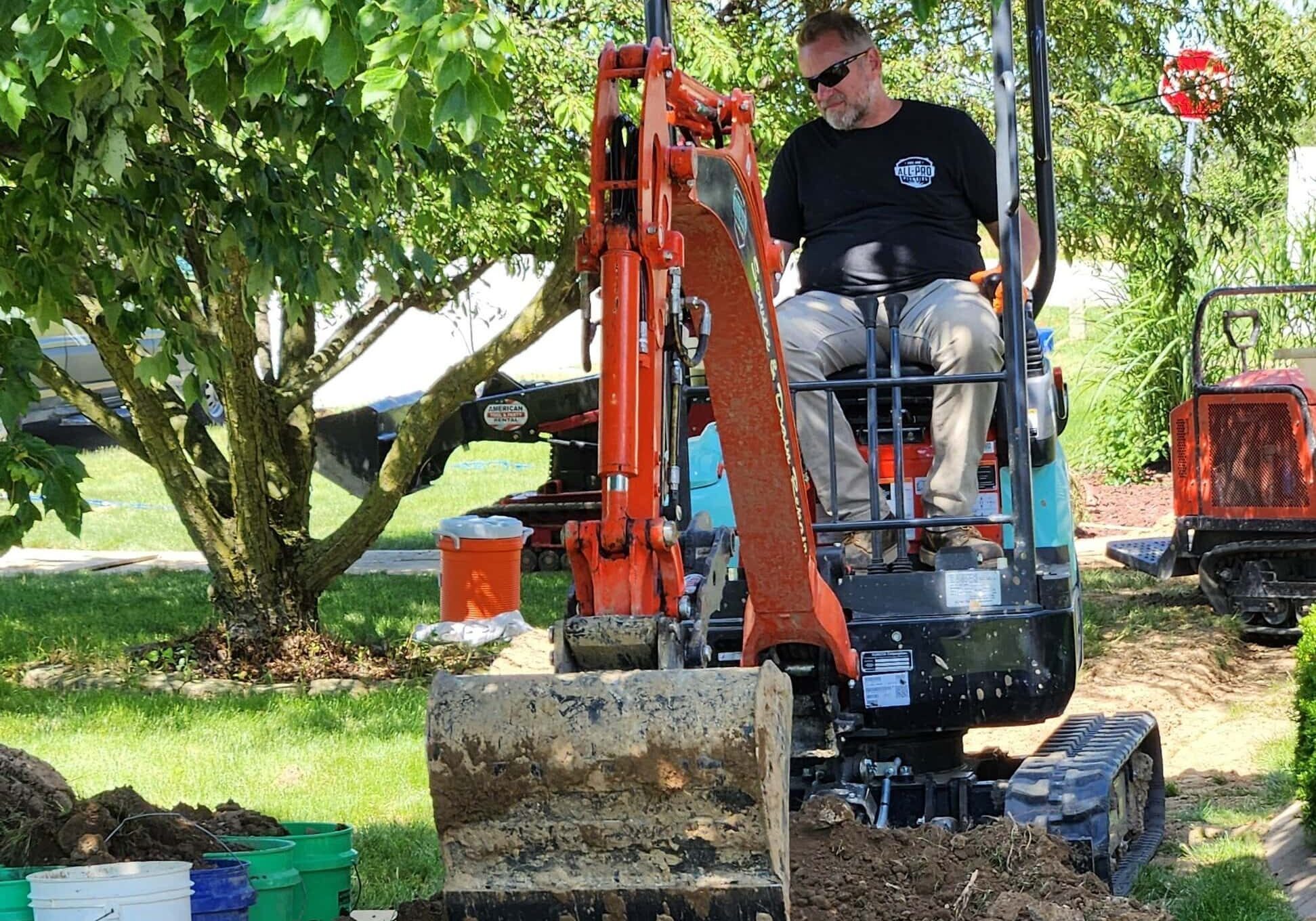 62-1 Excavator Drain Repair Dig Alert Perimeter Drain Sewer Tile Downspouts All-Pro Plumbing technician operating an excavator for traditional drain repair and perimeter drain or sewer line excavation at a residential site in Kokomo, IN