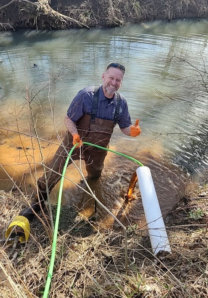 Master Plumber Terry standing in a creak smiling with a thumbs up as the geothermal drain clog breaks free and begins flowing freely from the use of powerful hydro jetting equipment.