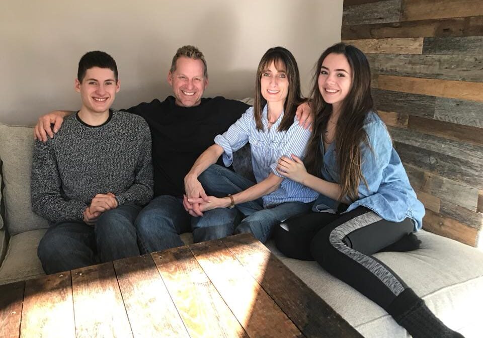 The Tracy family, owners of All-Pro Plumbing, smiling together indoors on a couch, representing the family-owned nature of the business in Kokomo, IN