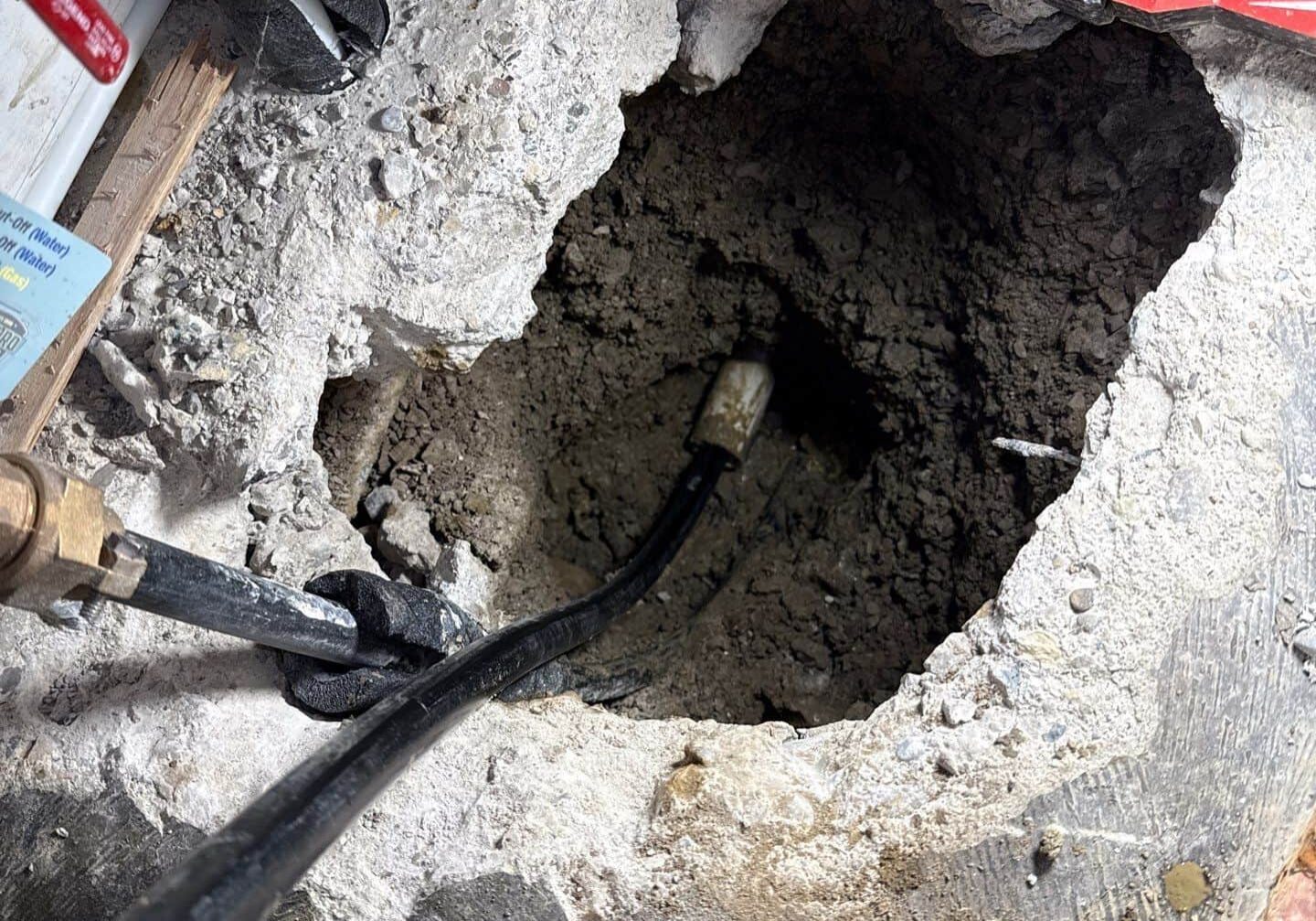 down-net_http20250807-117-ue0alv An excavated a hole in a concrete floor, revealing a water pipe with a leak underneath, representing slab leak detection and repair services by All-Pro Plumbing in Kokomo, IN