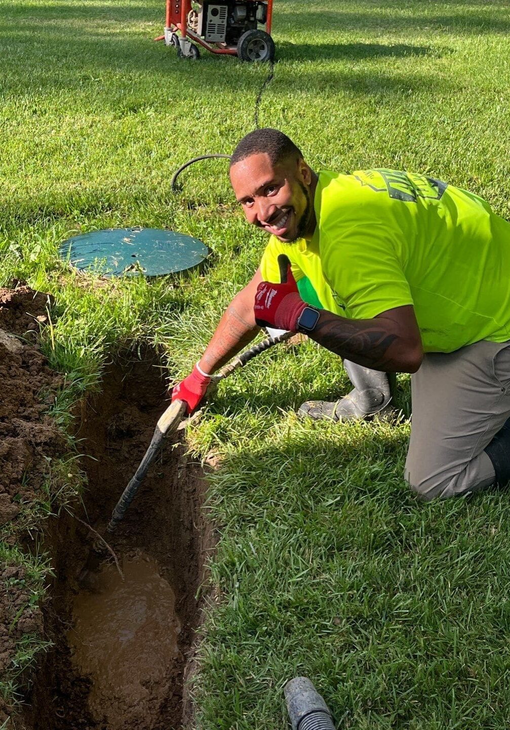All-Pro Plumbing technician kneeling in a trench for an outdoor drain repair, smiling and giving a thumbs up in Kokomo, IN