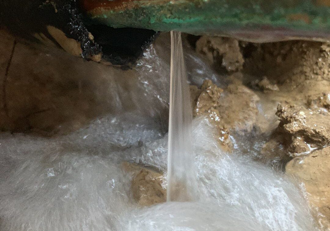 Underground burst pipe actively leaking water into muddy ground, indicating a severe plumbing leak requiring immediate repair from All-Pro Plumbing in Kokomo, IN