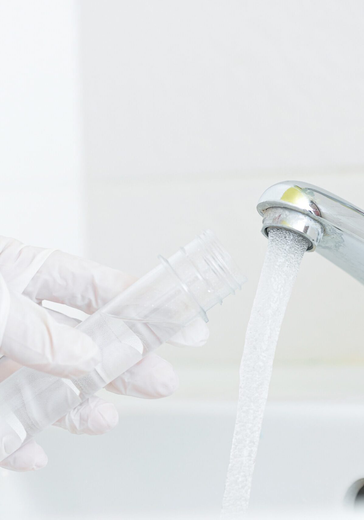 Gloved hand collecting a water sample from a bathroom faucet into a test tube, representing water quality testing for water treatment solutions by All-Pro Plumbing in Kokomo, IN