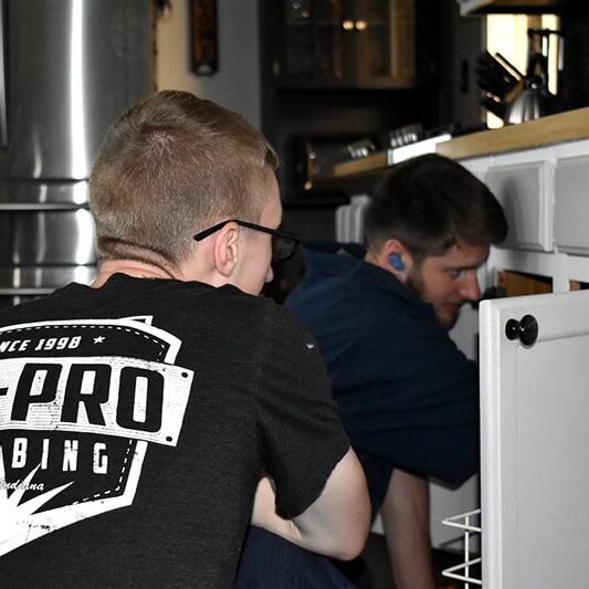 All-Pro Plumbing Kokomo IN Office lr Undersink Repair All-Pro Plumbing technician and apprentice working together on an undersink plumbing repair in a kitchen